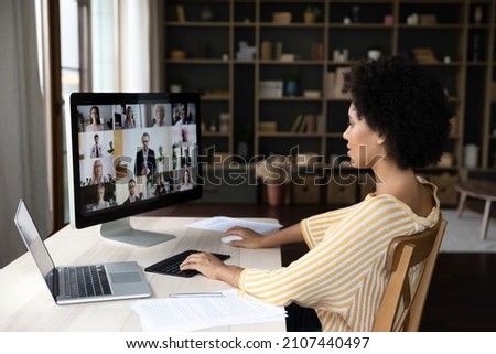 Side view concentrated millennial African American business woman holding video conference call conversation on computer with diverse colleagues, using different gadgets, sitting at table at workplace Royalty-Free Stock Photo #2107440497
