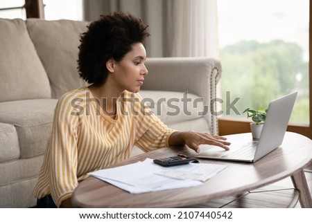Concentrated millennial smart African American woman using computer, paying for utility bills taxes online, planning investment, managing savings or monthly budget, financial accounting concept. Royalty-Free Stock Photo #2107440542
