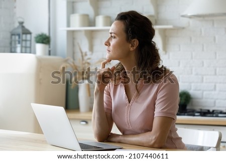 Pensive young stressed woman looking in distance, sitting at table with computer, thinking of received bad news in email, considering problem solution, feeling tired working remotely on online project