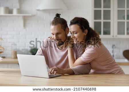 Affectionate loving millennial family couple using computer applications, reading email with good news, shopping online web surfing information, booking hotel or flight tickets, tech addiction.