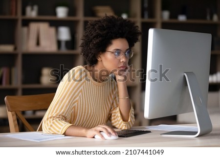 Thoughtful young African American business woman looking at computer monitor, feeling exhausted working on difficult tasks, considering project problem solution, analyzing data preparing document. Royalty-Free Stock Photo #2107441049