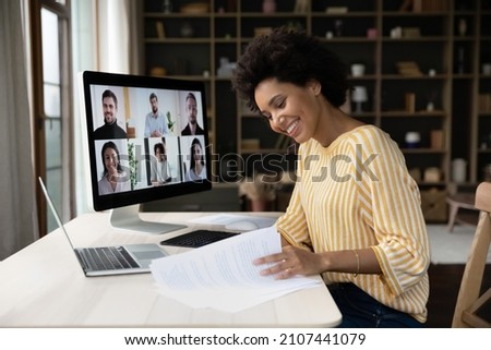 Side view focused smiling young African American female employee looking through paper documents, holding video conference call negotiations meeting with diverse colleagues business people online. Royalty-Free Stock Photo #2107441079
