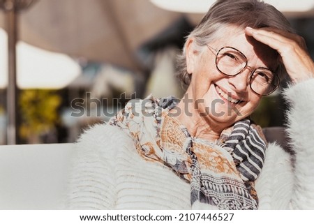 Portrait of happy attractive adult senior granny grandmother looking at camera under the sunlight wearing white sweater and scarf. Smiling retired woman with eyeglasses enjoying relaxed moments Royalty-Free Stock Photo #2107446527