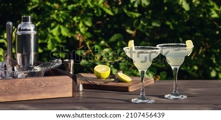 Two glasses with fresh homemade margarita cocktail on a wooden table on a patio summer evening, selective focus