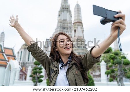 Asian woman backpacker use mobile phone selfie, take picture in city. Young girl tourist traveler travel alone on street use cellphone record vlog on holiday vacation trip in Buddha temple in Thailand