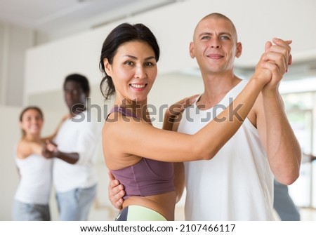 Smiling women and men practicing social dance moves in pair during group class