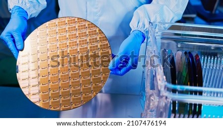 close up of asian male technician in sterile coverall holds wafer with gloves that reflects many different colors and check it at semiconductor manufacturing plant Royalty-Free Stock Photo #2107476194