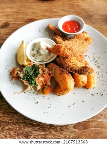 Fish and chips. Fried fish, potato chips, lime, vegetables salad, and tartare sauce on white plate
