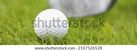Close-up of white golf ball and club laying on green grass. Macro shot of equipment for game. Competition and tournament. Fresh field for play. Luxury sport concept