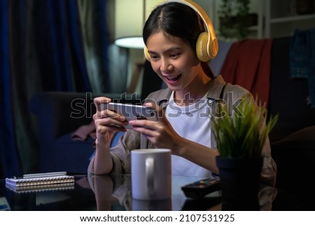 Excited Young Asian woman wearing headset and playing online game on smartphone with live broadcasting on internet. Royalty-Free Stock Photo #2107531925