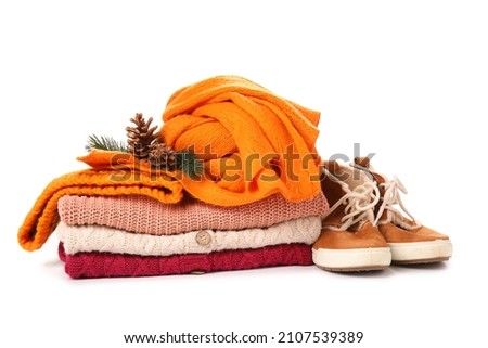 Stack of knitted sweaters, scarf, shoes and Christmas decor on white background