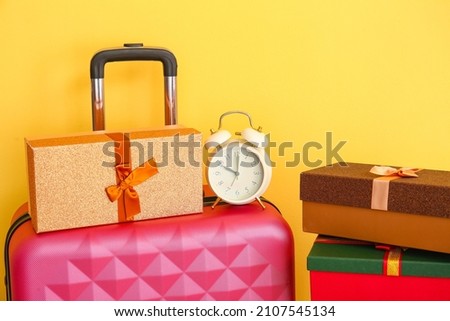 Suitcase, alarm clock and gift boxes on color background, closeup. Christmas vacation concept