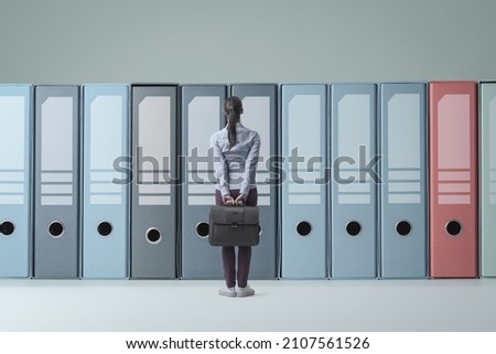 Confused businesswoman standing in front of huge ring binders in the archive, data management and storage concept Royalty-Free Stock Photo #2107561526