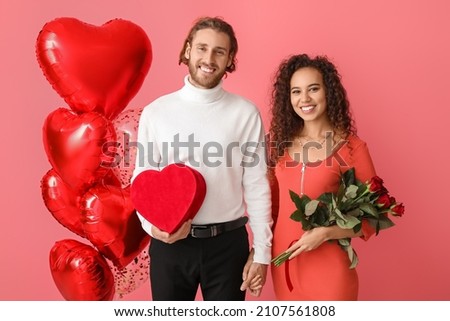 Happy young couple with balloons, gift and flowers on color background. Valentine's Day celebration