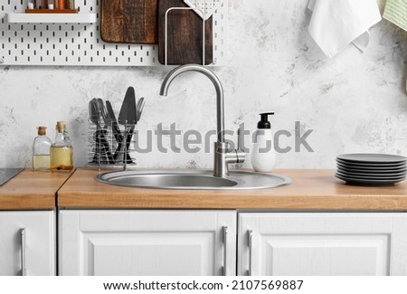 Wooden counter with silver sink and utensils near light wall in kitchen Royalty-Free Stock Photo #2107569887