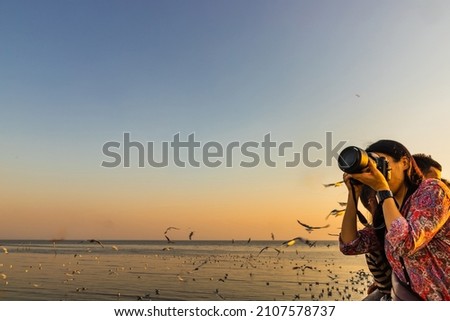 Asian woman taking photo seagulls at Bangpu seaside. Thailand. No focus, specifically.