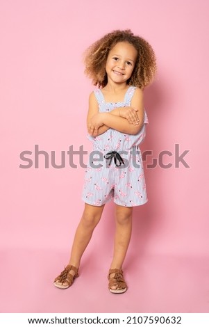 Full length photo of excited charming cute little girl with her hands folded standing over pink background.