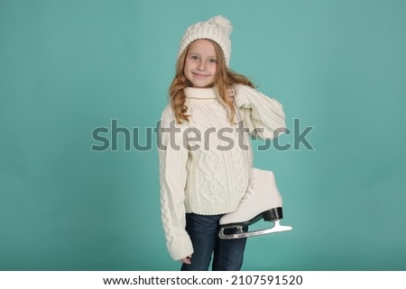 a blonde girl in a white knitted sweater and a white hat holds white figure skating skates in her hands