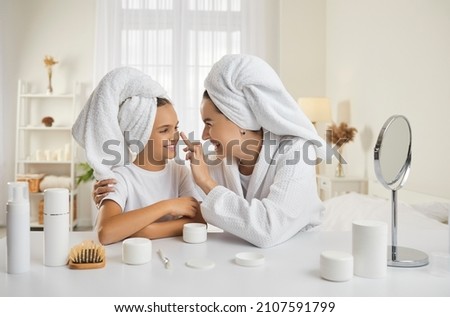 Mother and child having fun during skin care routine. Happy beautiful mommy and pretty little daughter sitting at beauty table, enjoying self care, applying face cream and having good time together Royalty-Free Stock Photo #2107591799