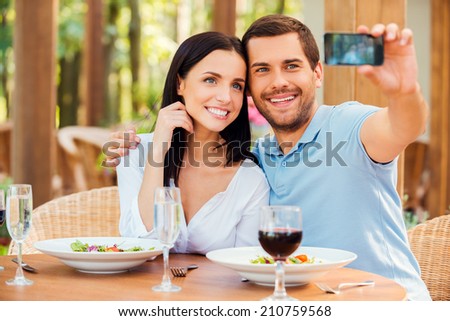 Making selfie in restaurant. Beautiful young loving couple making selfie with mobile phone and smiling while relaxing in outdoors restaurant together 