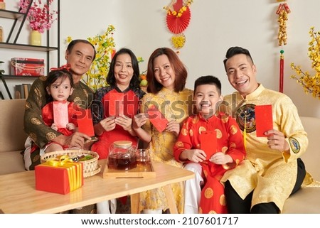 Smiling family members in ao dai dresses holding red lucky money envelopes Royalty-Free Stock Photo #2107601717
