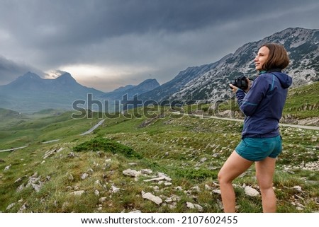 Young woman with camera enjoying dramatic view of mountains of Durmitor, Montenegro on storm day.
