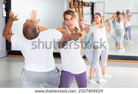 Young Latina paired up with male partner in self defense training, practicing elbow hit in close combat