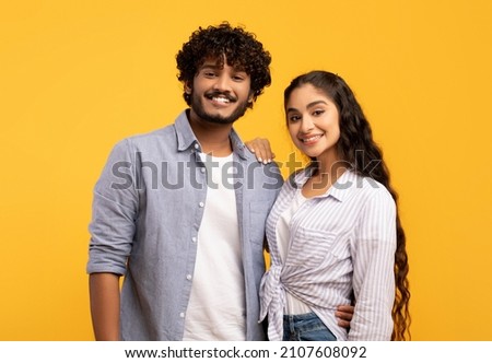 Romantic couple. Portrait of happy indian man and woman embracing on yellow background, young spouses hugging and smiling at camera, posing in studio