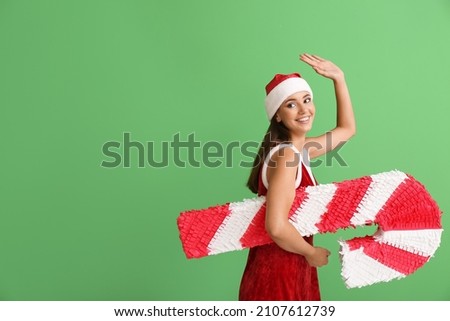 Beautiful woman dressed as Santa with candy cane pinata on color background