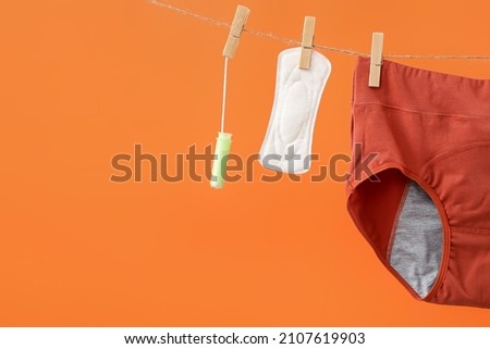 Period panties, tampon and pad hanging on rope against color background, closeup