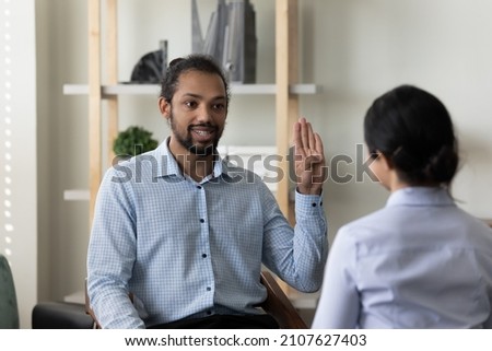 Happy millennial handsome African American man with hearing disability making gestures, using sign language practicing communication with professional female Indian therapist in clinic office. Royalty-Free Stock Photo #2107627403