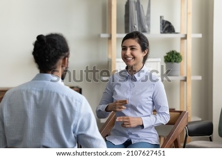 Smiling young Indian woman with hearing disability making gestures with fingers, communicating with African American friend or involved in curing therapy with skilled male doctor in clinic office. Royalty-Free Stock Photo #2107627451