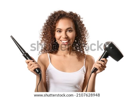 Young African-American woman with hair dryer and curling iron on white background