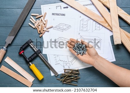 Woman holding nuts with bolts, furniture assembling instructions and tools on color wooden background Royalty-Free Stock Photo #2107632704