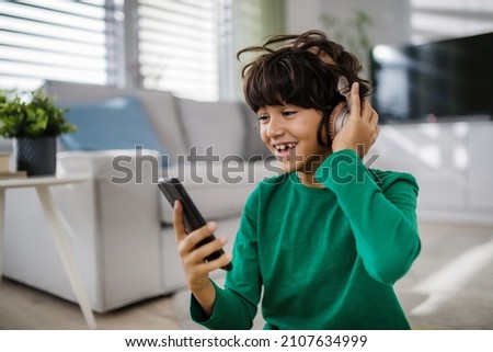 Happy multiracial boy with headphones and smartphone listening to music at home.