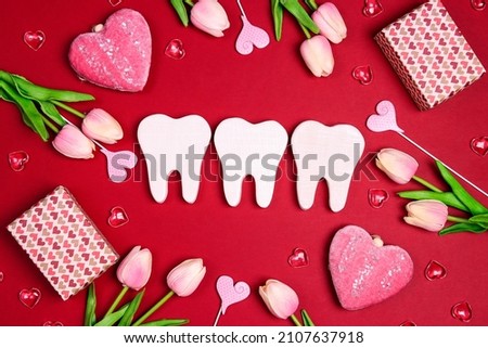 White teeth surrounded by gifts, hearts and tulip flowers on a red background. Dental Valentine card. Valentine's day concept.  