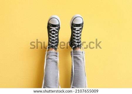 Legs of woman in black sneakers with untied white laces on yellow background