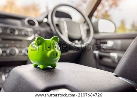 Green piggy bank money box in car interior, vehicle purchase, insurance or driving and motoring cost Royalty-Free Stock Photo #2107664726
