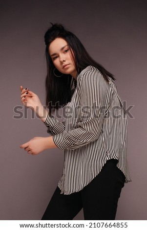  brunette hair modern girl in black and white strips shirt and black pants outfit stand and posing indoor pink background looking away