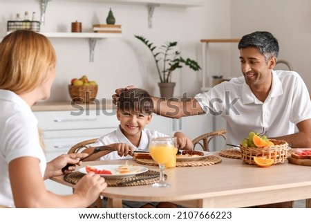 Happy family with little son having breakfast at table in kitchen