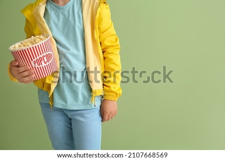 Little boy with bucket of tasty popcorn on green background
