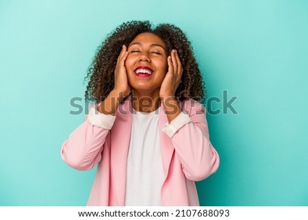 Young african american woman with curly hair isolated on blue background laughs joyfully keeping hands on head. Happiness concept.
