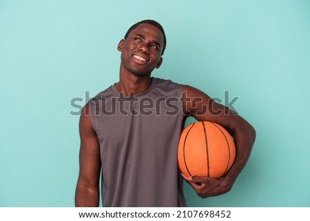Young African American man playing basketball isolated on blue background dreaming of achieving goals and purposes