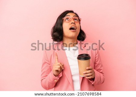 Young latin woman holding take away coffee isolated on pink background pointing upside with opened mouth.