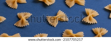 Uncooked farfalle pasta on dark navy background banner. Macaroni background. Top view, flat lay. 
