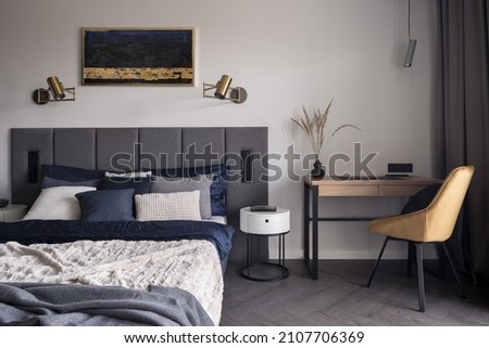 Comfortable and stylish bedroom with cozy bed, stylish bedclothes and functional desk with yellow chair Royalty-Free Stock Photo #2107706369