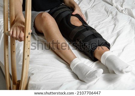 Female patient wearing orthosis sitting on bed holding crutches after surgery on broken leg. Rehabilitation of injured woman at home. Selective focus Royalty-Free Stock Photo #2107706447