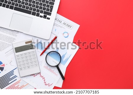 Calculator with magnifier, laptop and charts on red background