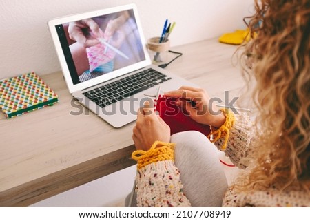 Back view of woman at home following a tutorial channel on laptop computer to learn knitting work wool activity for her hobbies or job - Close up of female knitting wool activity with internet class  Royalty-Free Stock Photo #2107708949