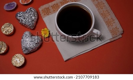 still life with silver hearts with a yellow flower and a colored fan with black lace and a cup of coffee with a spoon in the form of a lilac treble clef on a saucer on a red background is a symbol of 